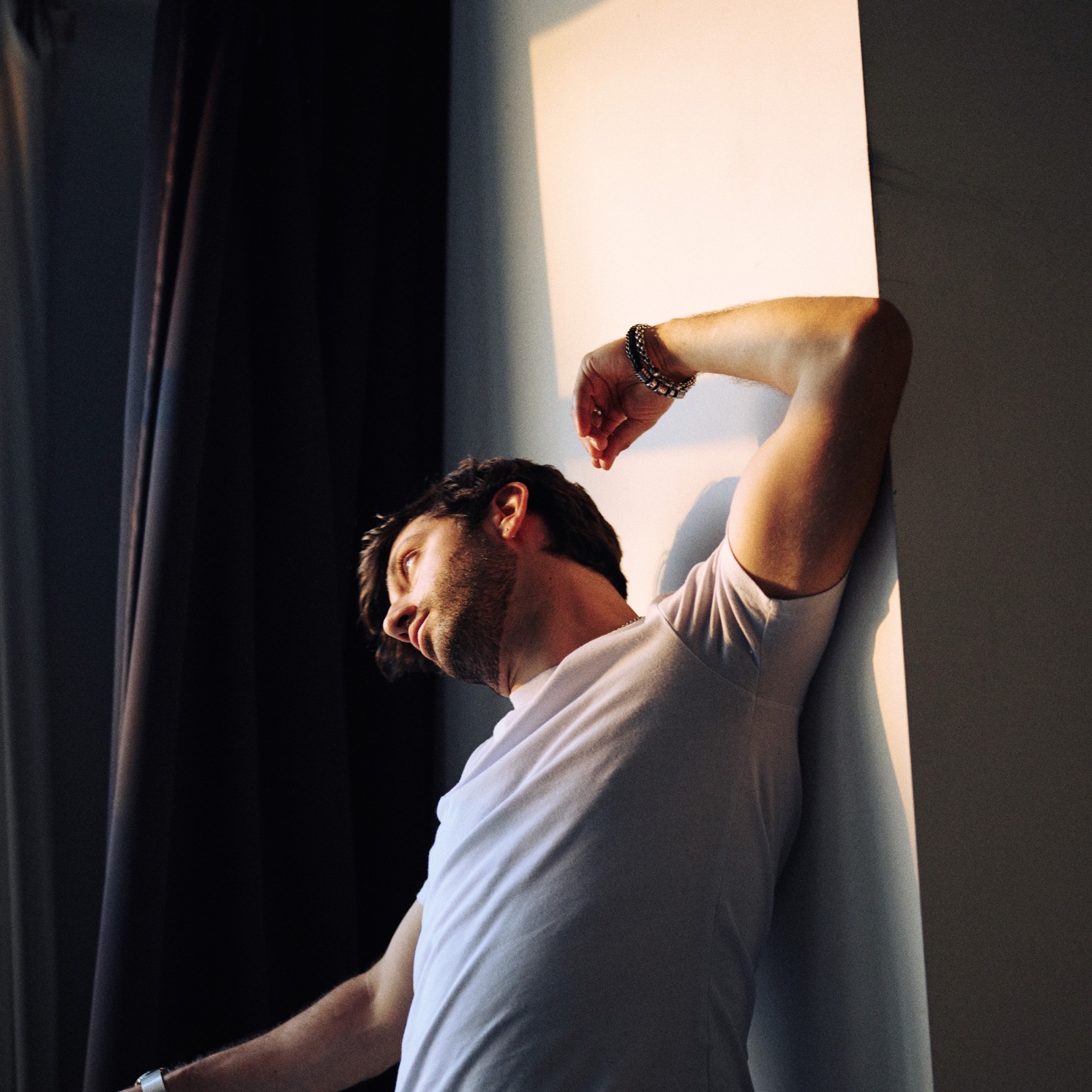 Sam Haiman leaning against a wall in hard raking daylight